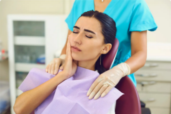 Patient in dental chair holding face in pain while dentist in scrubs offers support before emergency treatment.